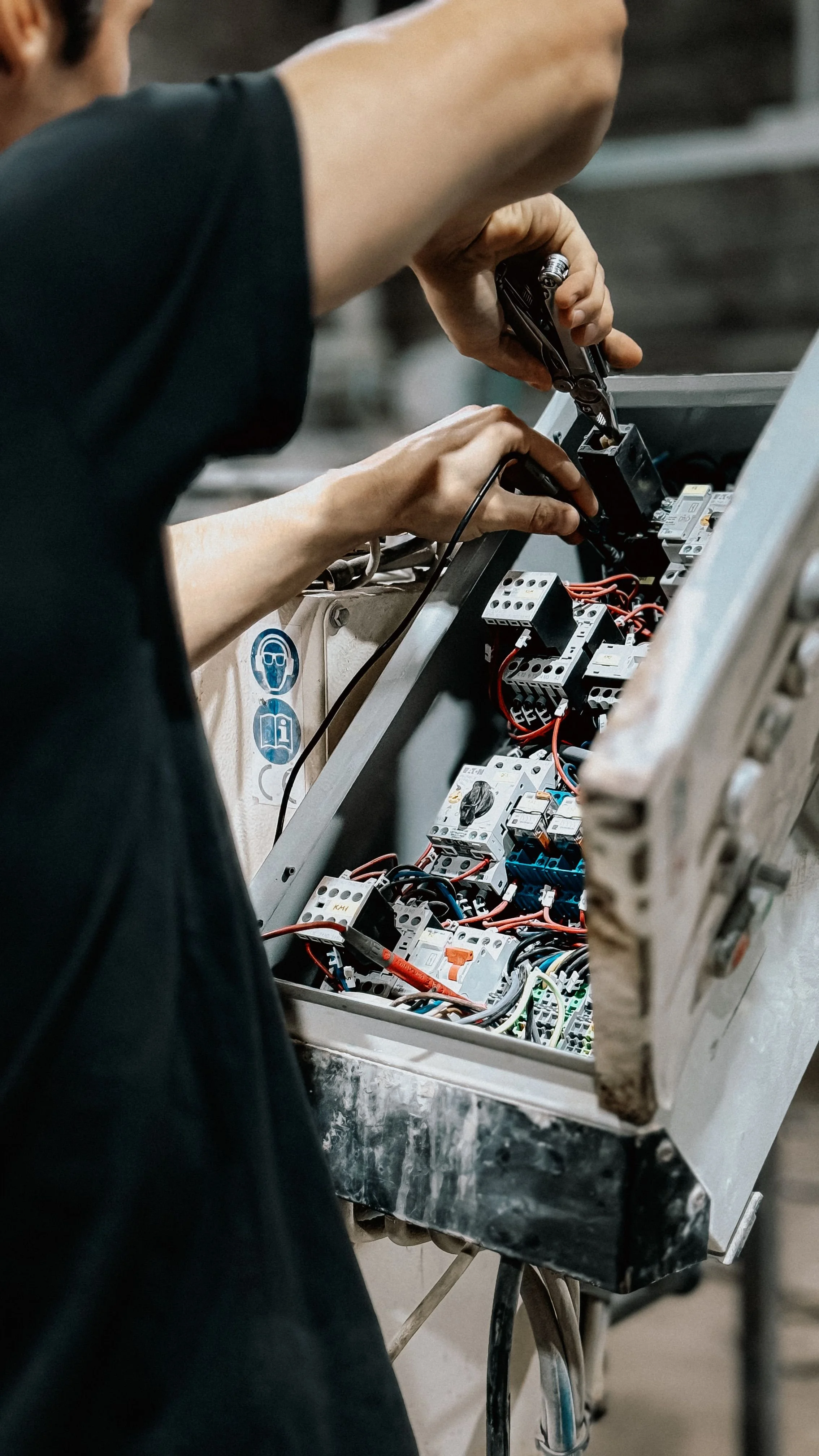 Person working on electrical wiring inside an open control panel with various wires and components.