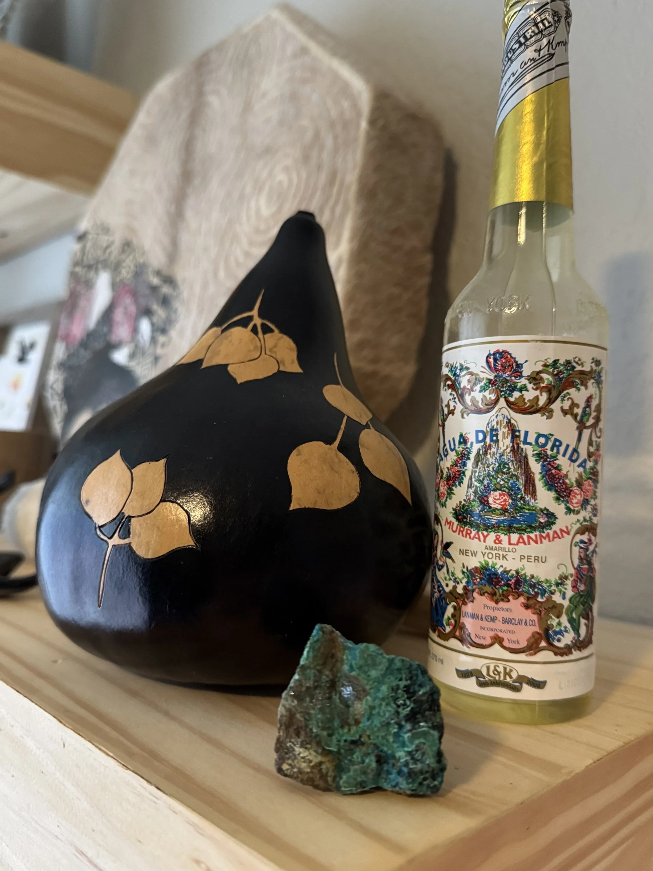 Decorative black vase with gold floral design, a piece of rough turquoise mineral, and a bottle of Agua de Florida perfume on a wooden surface.