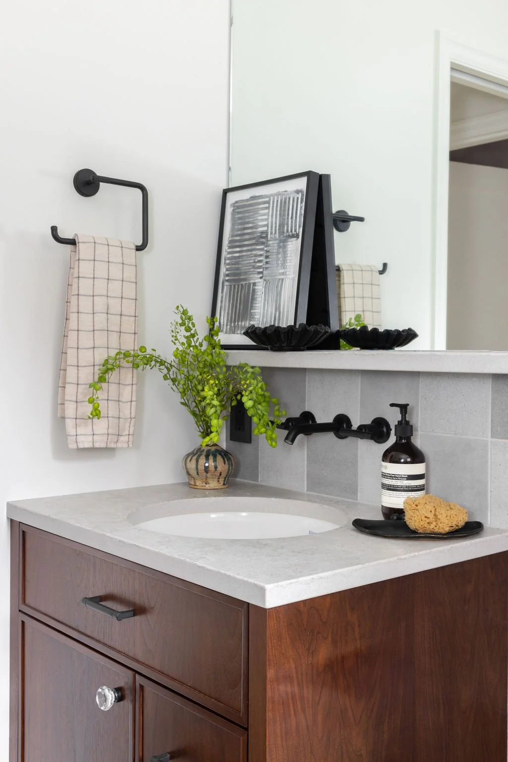 Seattle Bathroom Remodel. Seattle Design Firm. Bathroom vanity with a white countertop, round sink, black faucet, brown wooden cabinet, a small green plant in a pot, two black bowls, and a soap dispenser, mirror.