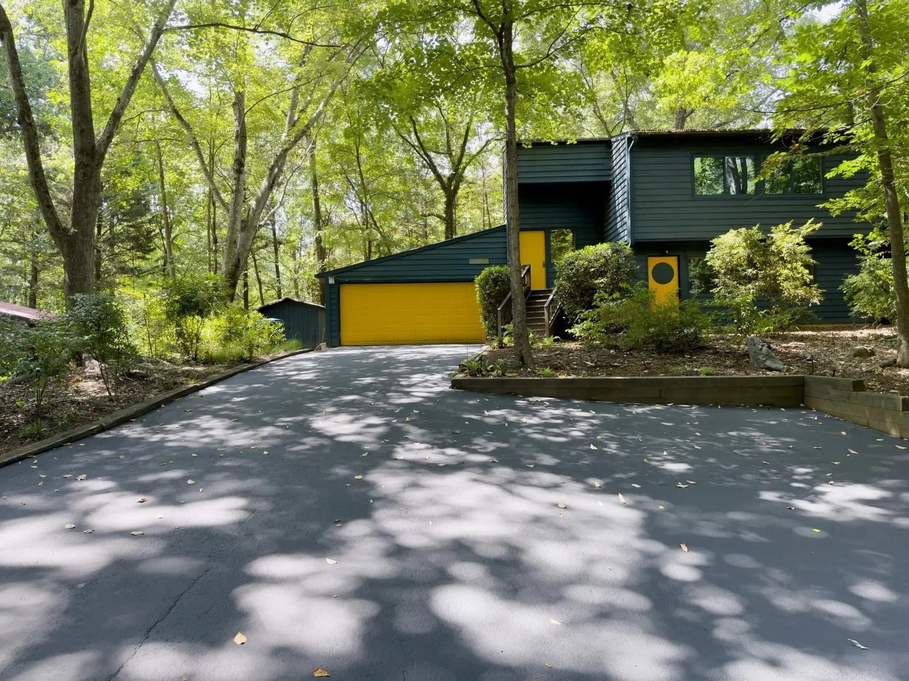 Freshly sealcoated asphalt driveway leading to a two-story home, shaded by mature trees