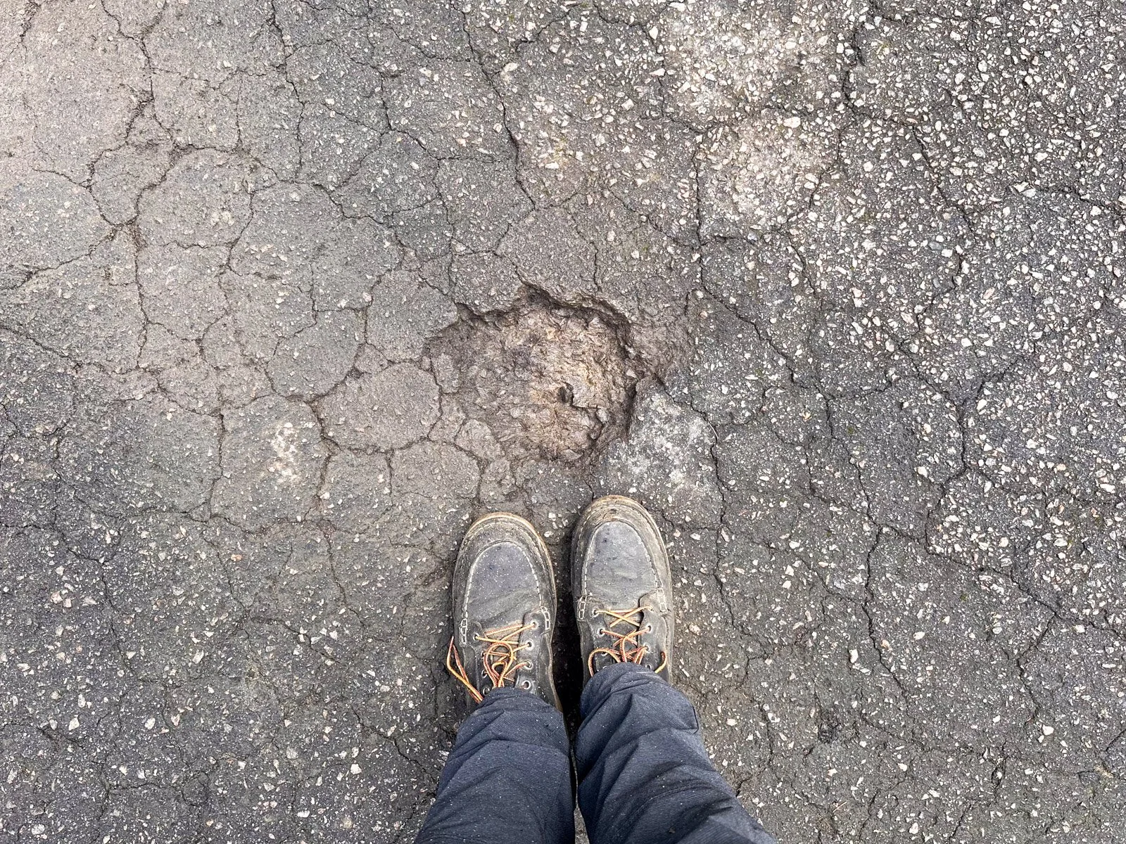 Unrepaired pothole in cracked, weathered asphalt pavement before a throw-and-roll patch repair in Durham, NC.