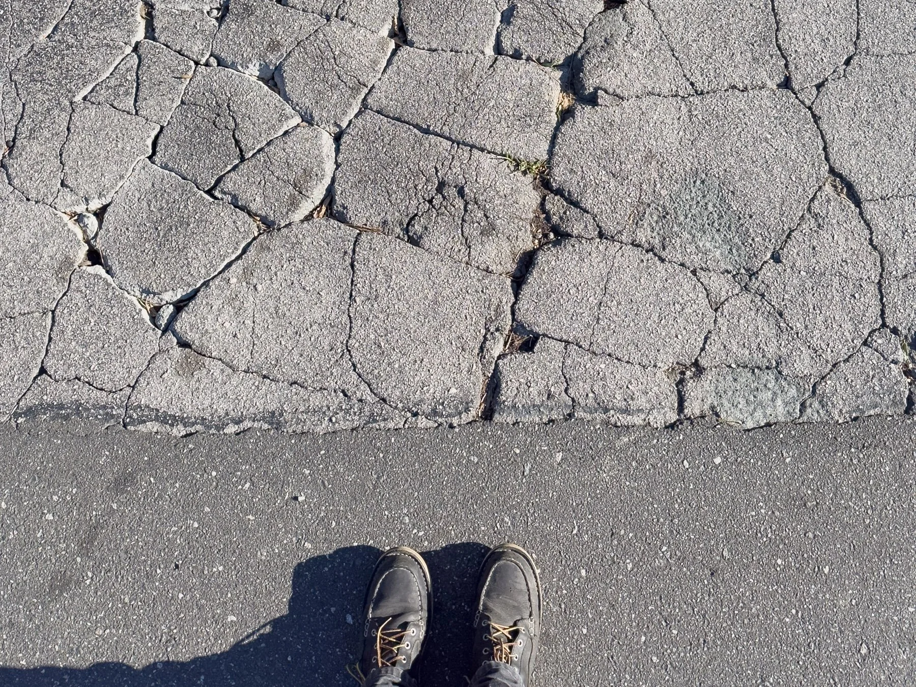 Alligator-cracked asphalt before infrared pothole repair in Durham, NC, with a crew member's work boots visible beside the damaged pavement