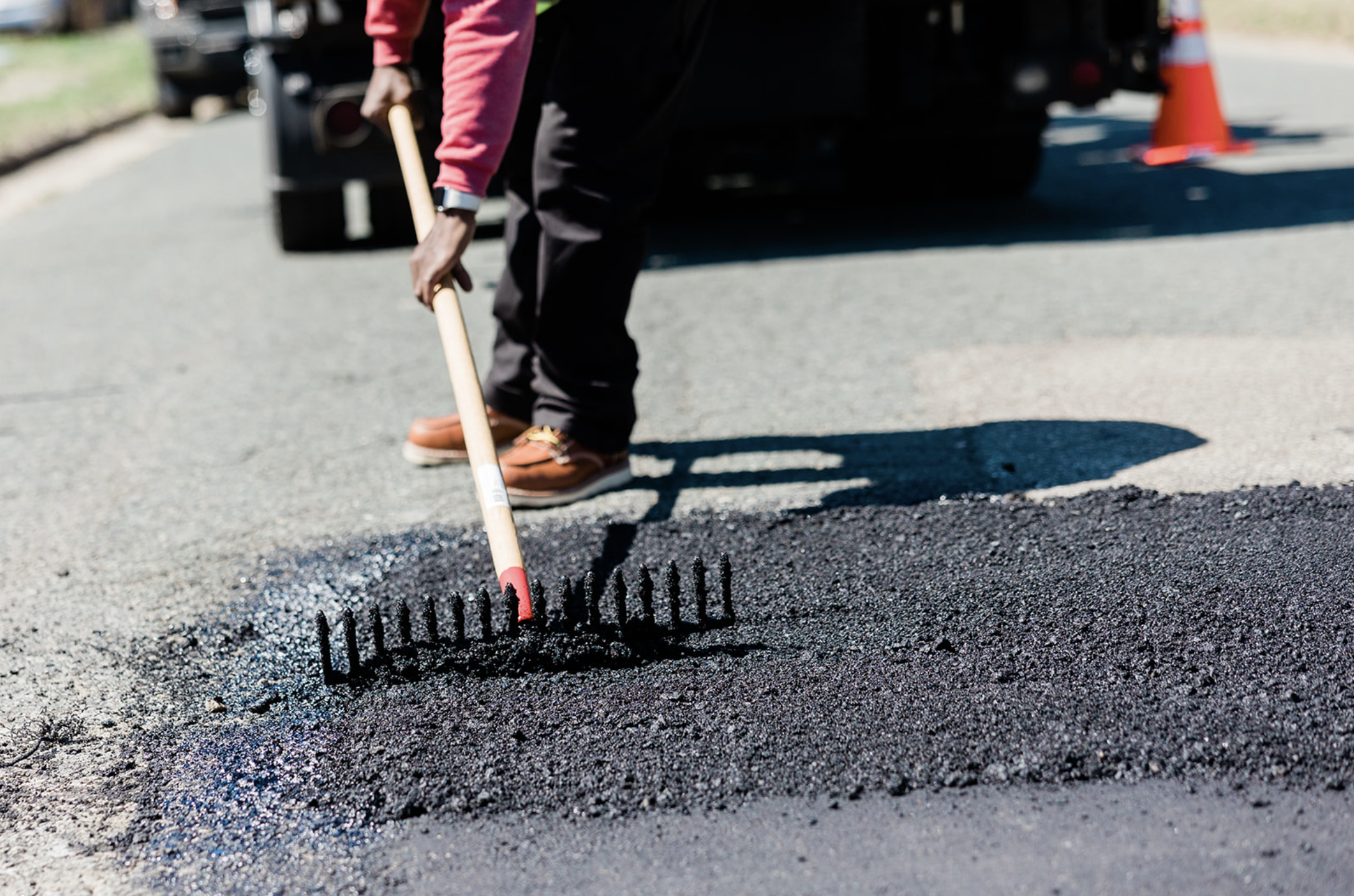 Person using a rake to spread fresh asphalt on a road surface during paving work in Durham, NC.