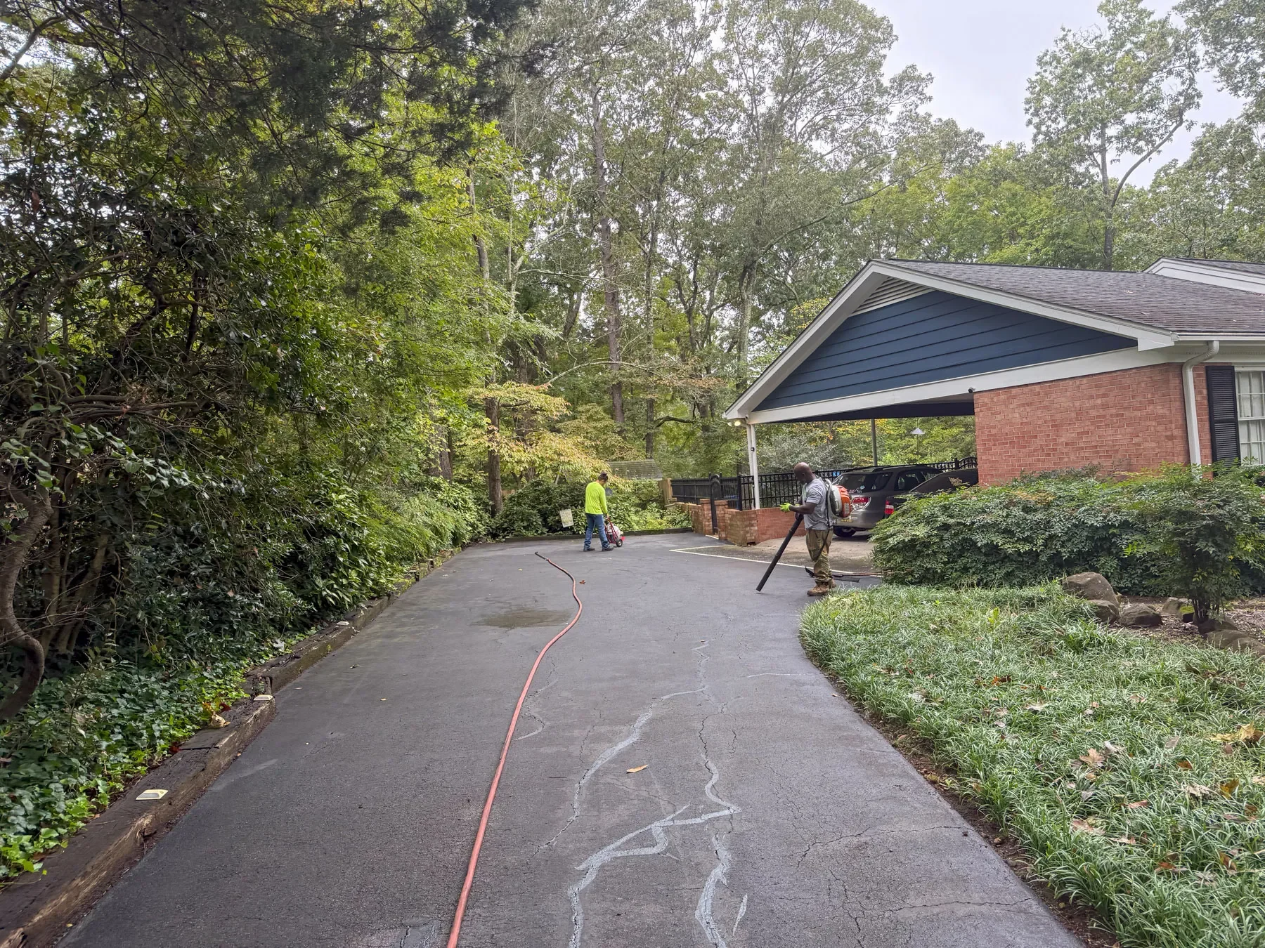 Two Green Street Blacktop crew members preparing a residential driveway for sealcoating, one blowing off debris and the other guiding the hose.