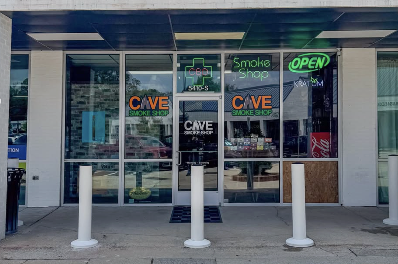 Front entrance of a smoke shop protected by three white bollards installed by Green Street Blacktop. Glass door with reflections of cars and surroundings outside.