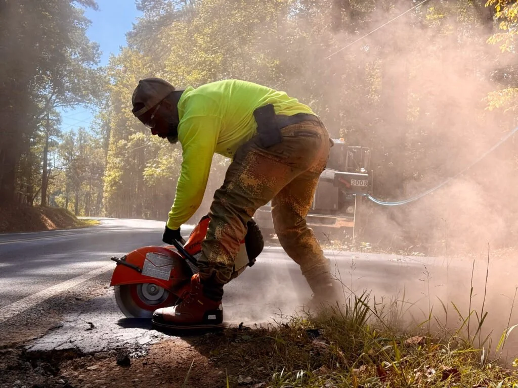 A Green Street Blacktop crew member cuts asphalt pavement with a handheld saw, Durham NC