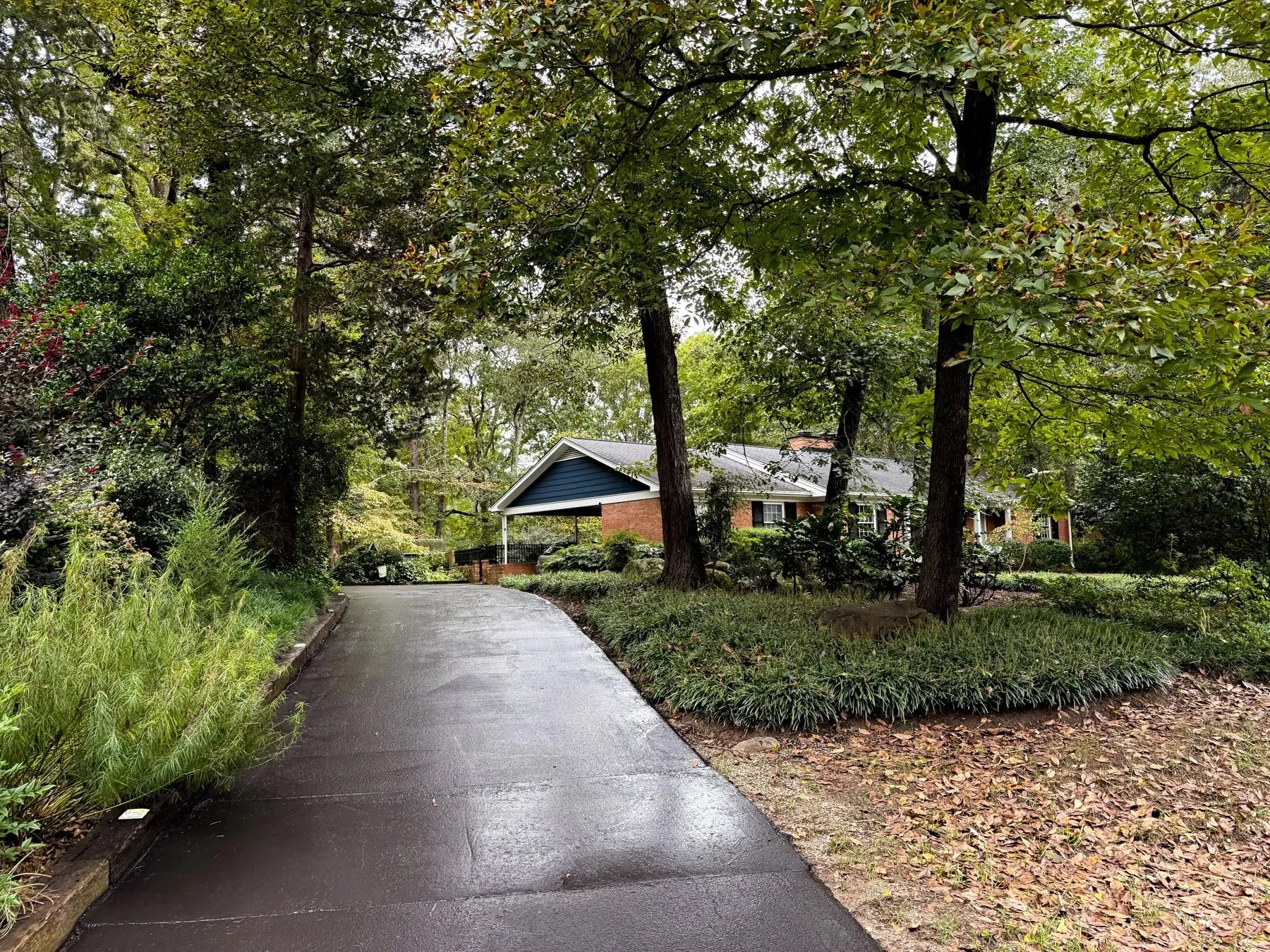 The same Durham, NC driveway freshly sealcoated, with a smooth, dark black finish winding through wooded landscaping to the home