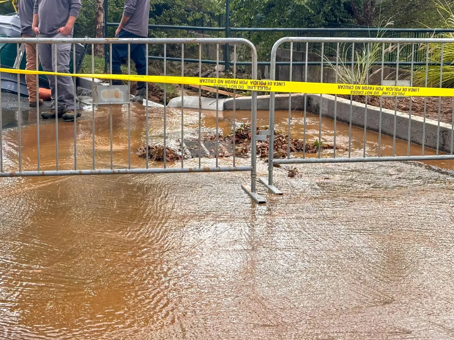Muddy stormwater flooding pooling around a storm drain catch basin, cordoned off with caution tape after heavy rain in Durham, NC