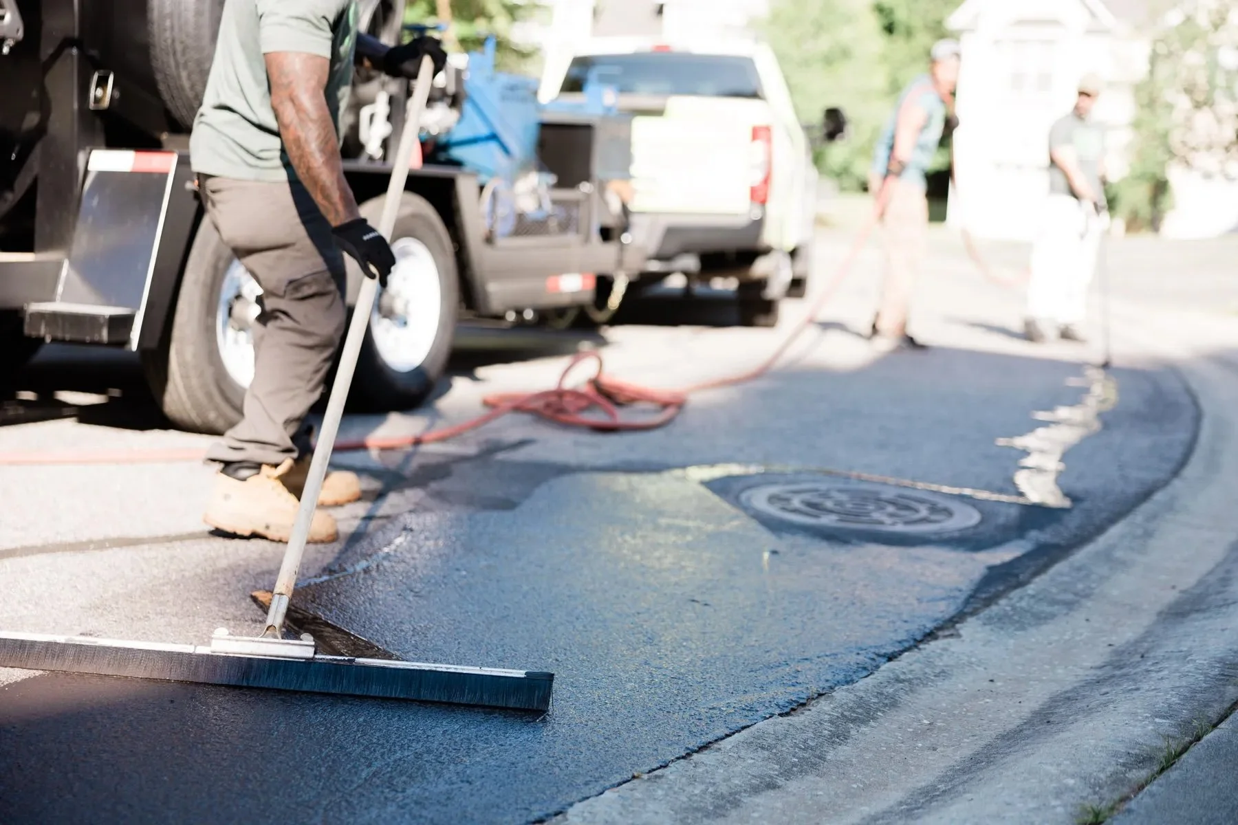 A Green Street Blacktop crew member spreads fresh sealcoat with a squeegee broom during a street sealcoating project in Durham, NC