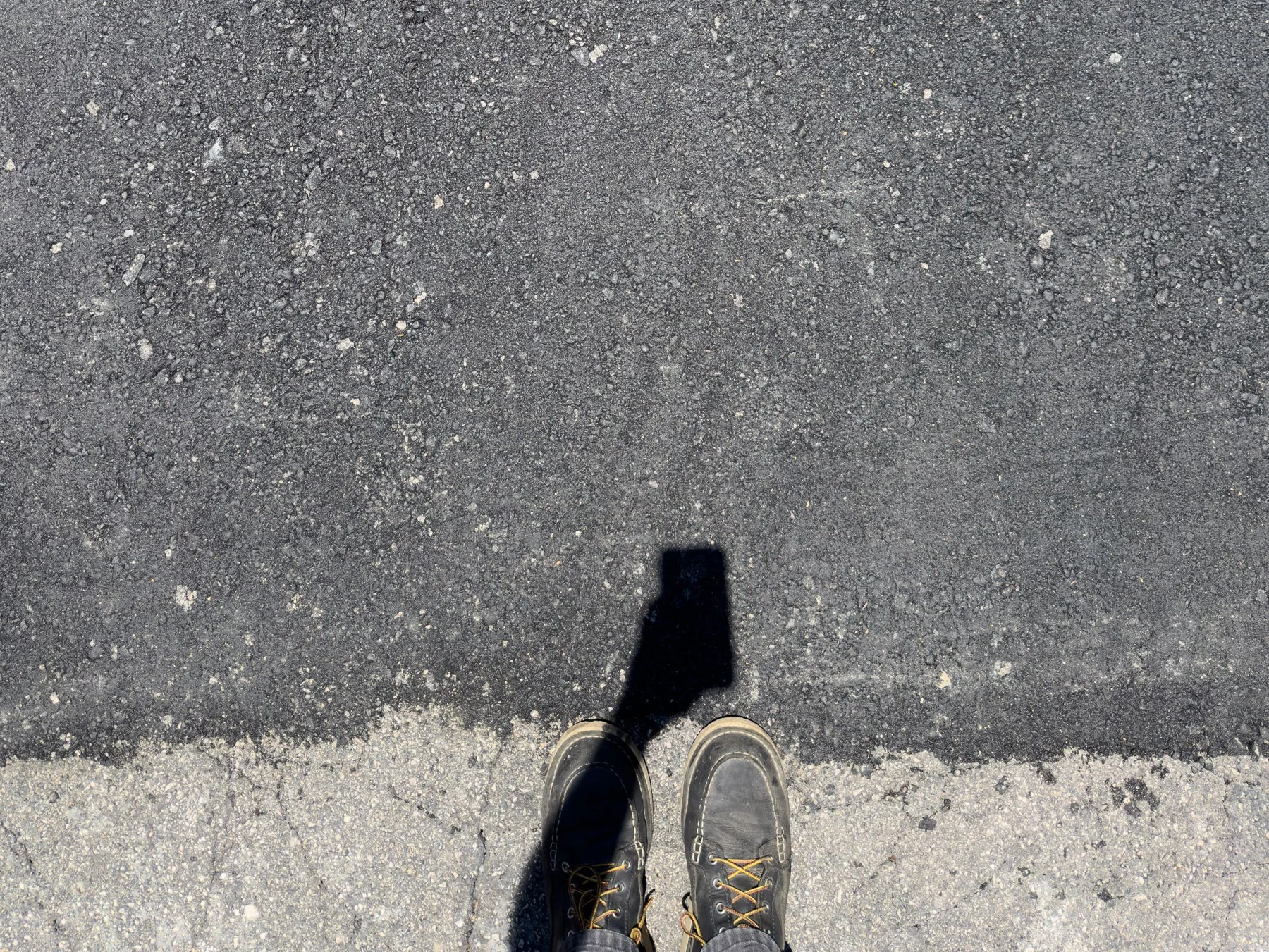 Smooth, seamless asphalt after infrared pothole repair in Durham, NC, with a worker's boots visible at the edge of the repair.