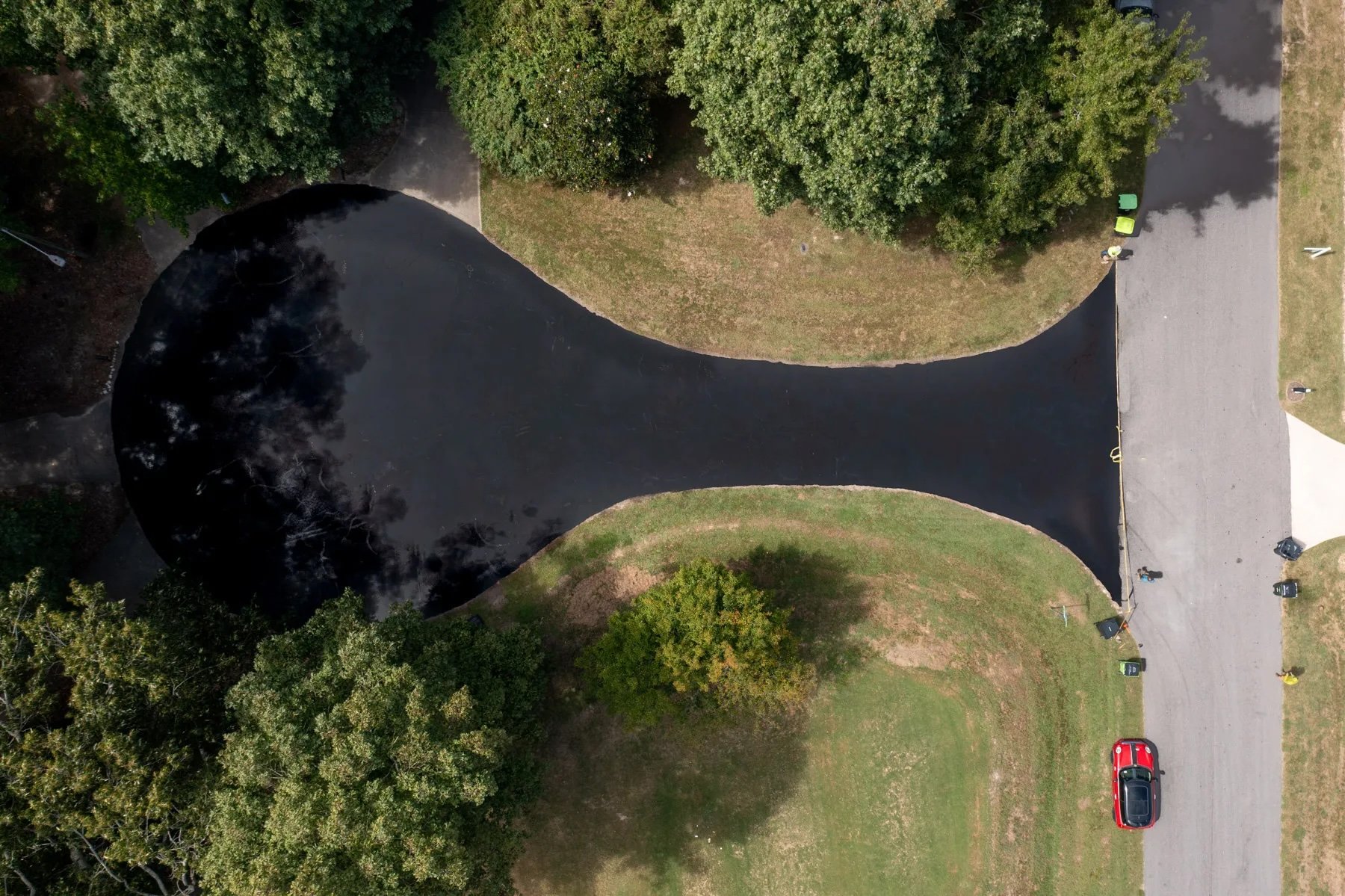 Aerial view of a freshly sealcoated cul-de-sac in the Cary/Apex, NC area, its deep black finish standing out against the surrounding lawn and trees.