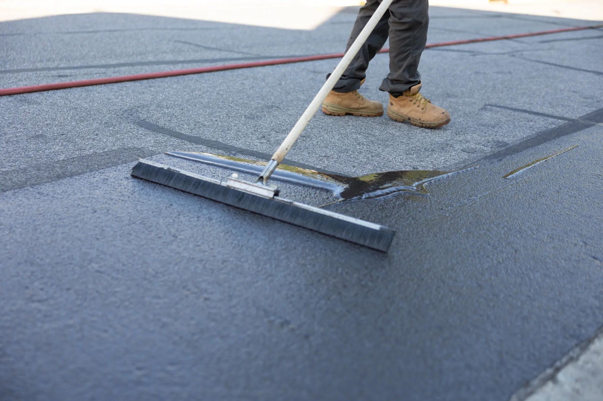 Green Street Blacktop employee using a squeegee to apply fresh asphalt sealcoat to a driveway surface in Chapel Hill, NC.