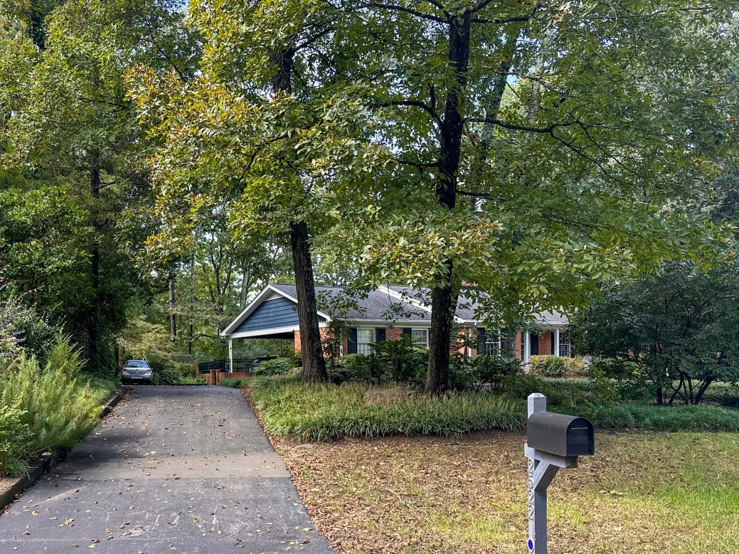 A long, tree-shaded driveway leading to a brick ranch home in Durham, NC, showing worn asphalt before sealcoating.