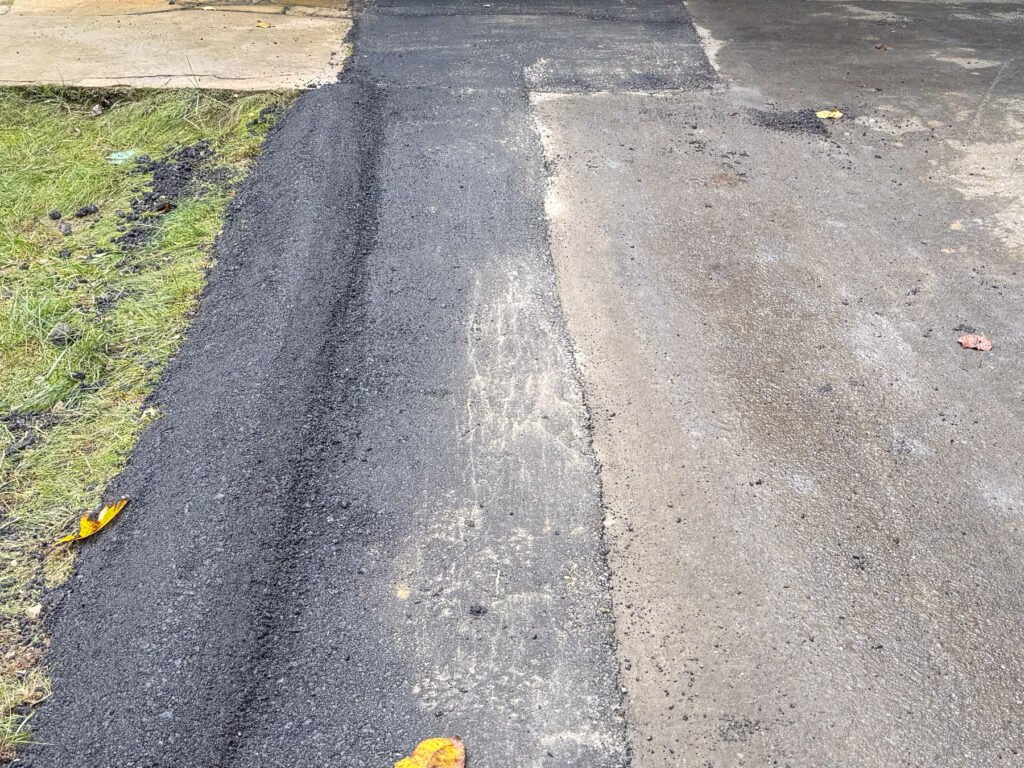Freshly patched dark asphalt strip running along a curb, next to the older surrounding pavement