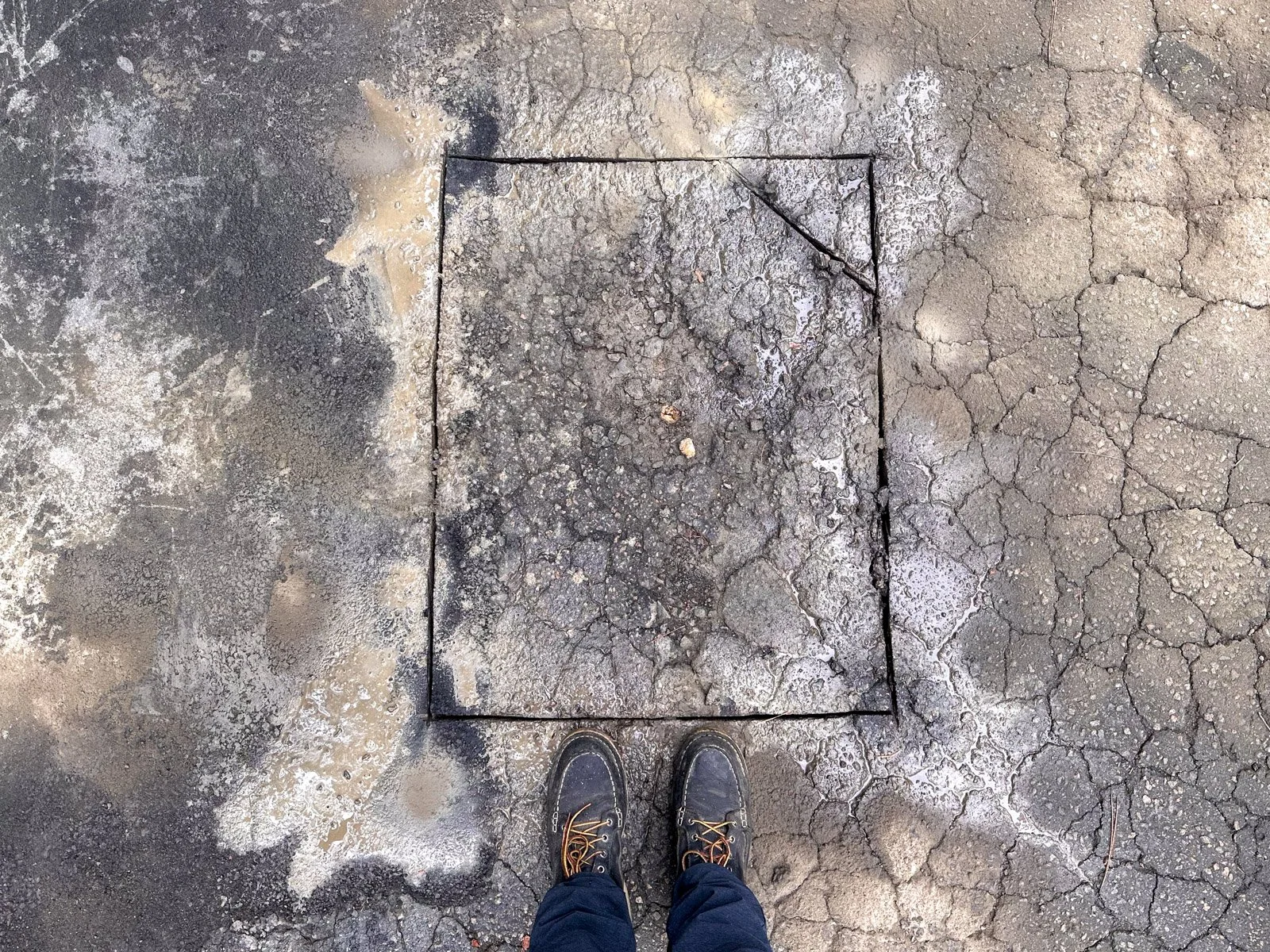 Square saw-cut outline around a damaged section of asphalt before a cut-and-patch pothole repair in Durham, NC.