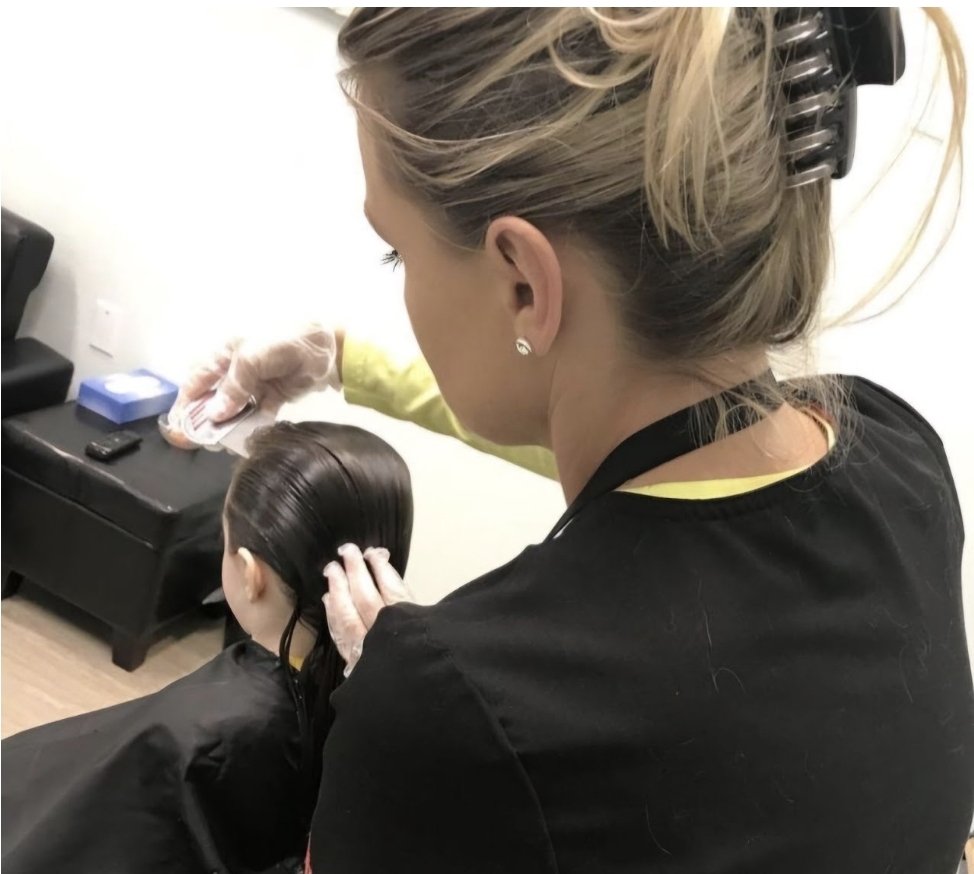 A hairstylist applies hair dye or treatment to a woman's long, dark, and wet hair in a salon setting.