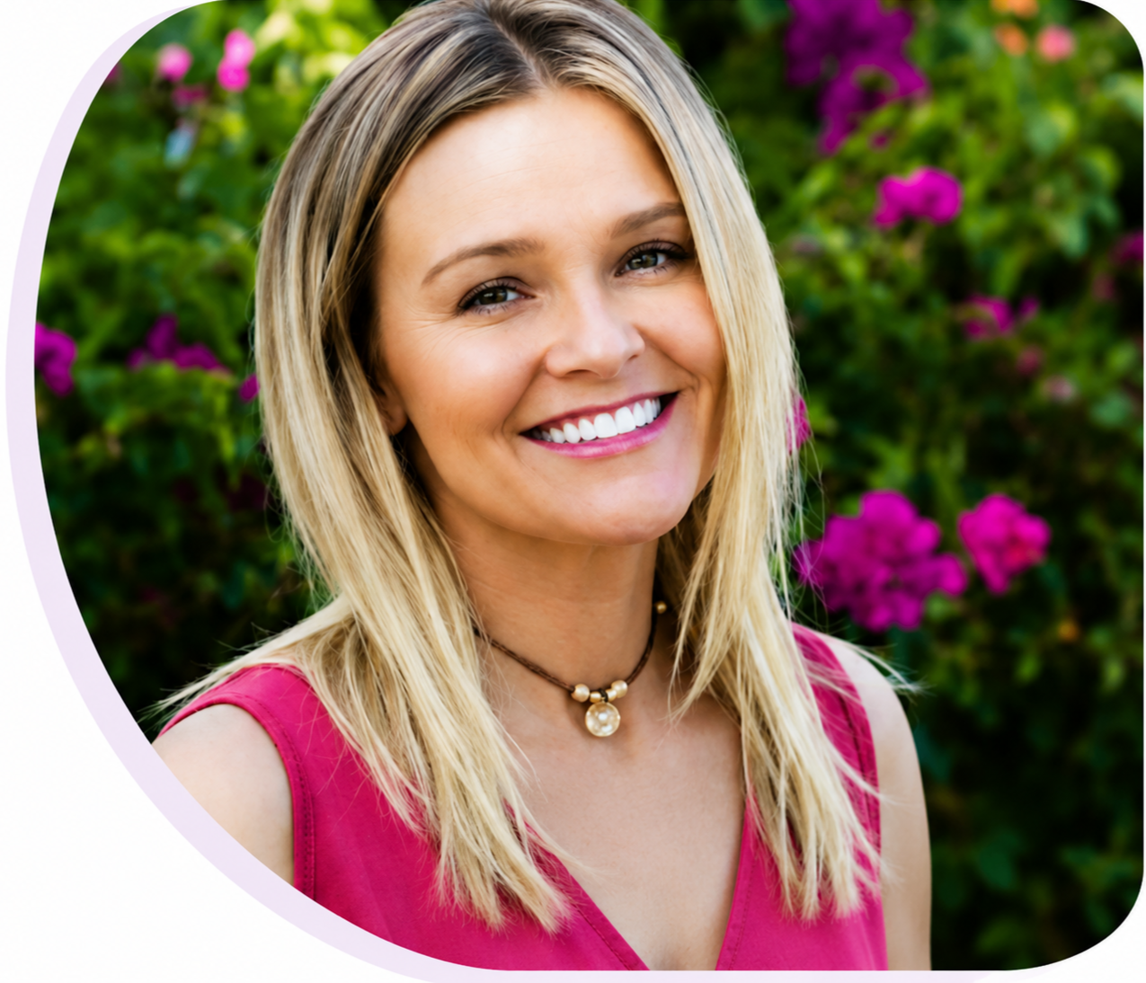 A smiling woman with blonde hair, wearing a pink sleeveless top and a beaded necklace, standing in front of a lush green background with pink flowers.