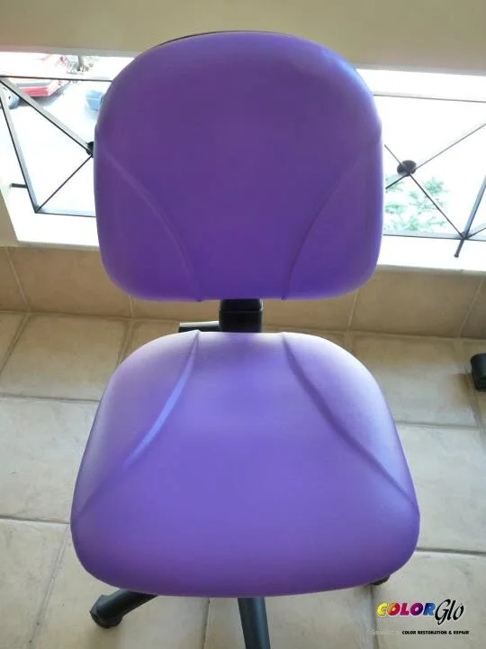A purple office or desk chair with a padded backrest and seat, positioned in front of a window with a view outside.
