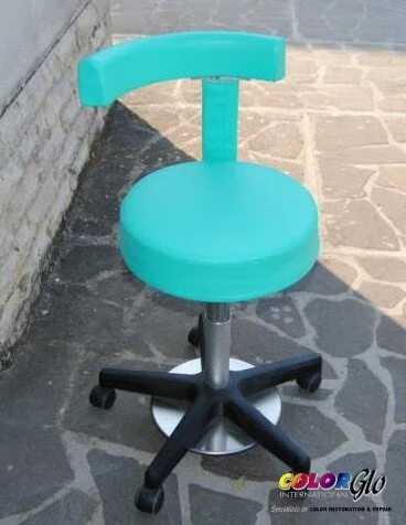 A turquoise office chair with a round cushion seat, backrest, and black base with wheels, placed on a stone patio next to a brick wall.