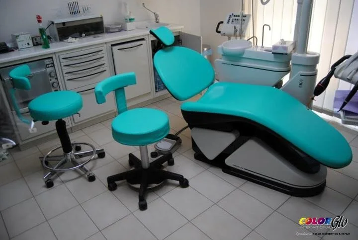 Dental treatment room with teal-colored dental chair, dental stools, and various dental equipment in the background.