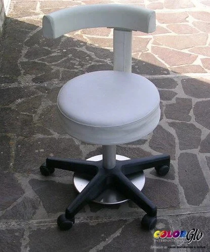 A white, modern office or desk chair with a round seat on a five-wheel black base, placed on a stone-paved outdoor surface.