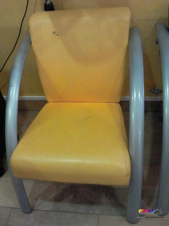 Yellow chair with metal armrests and legs, placed against a wall, showing signs of wear with some stains and scratches.