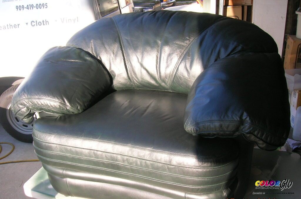 A black leather couch with oversized, plush armrests in a garage or storage area.