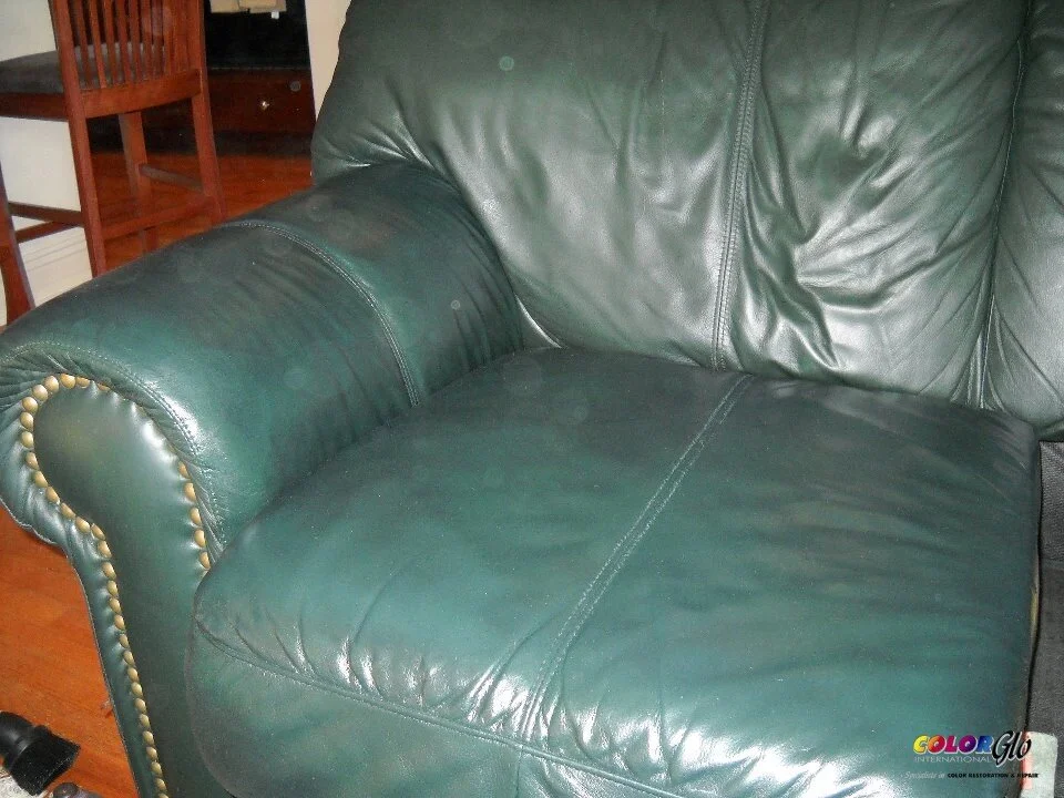 Close-up of a dark green leather armchair with brass nailhead trim on the armrest, in a living room setting.