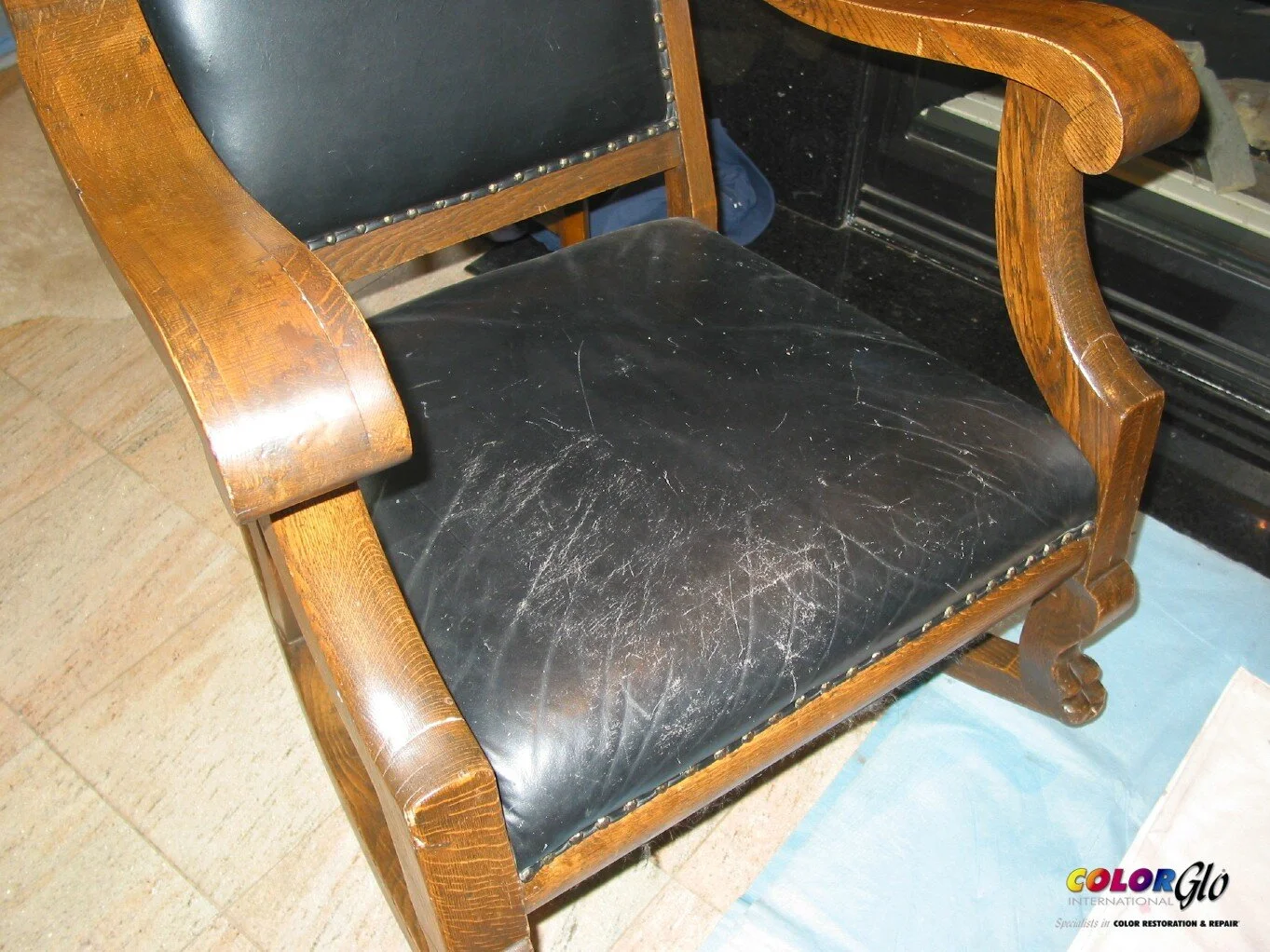 Wooden armchair with black leather upholstery that is scratched and worn.
