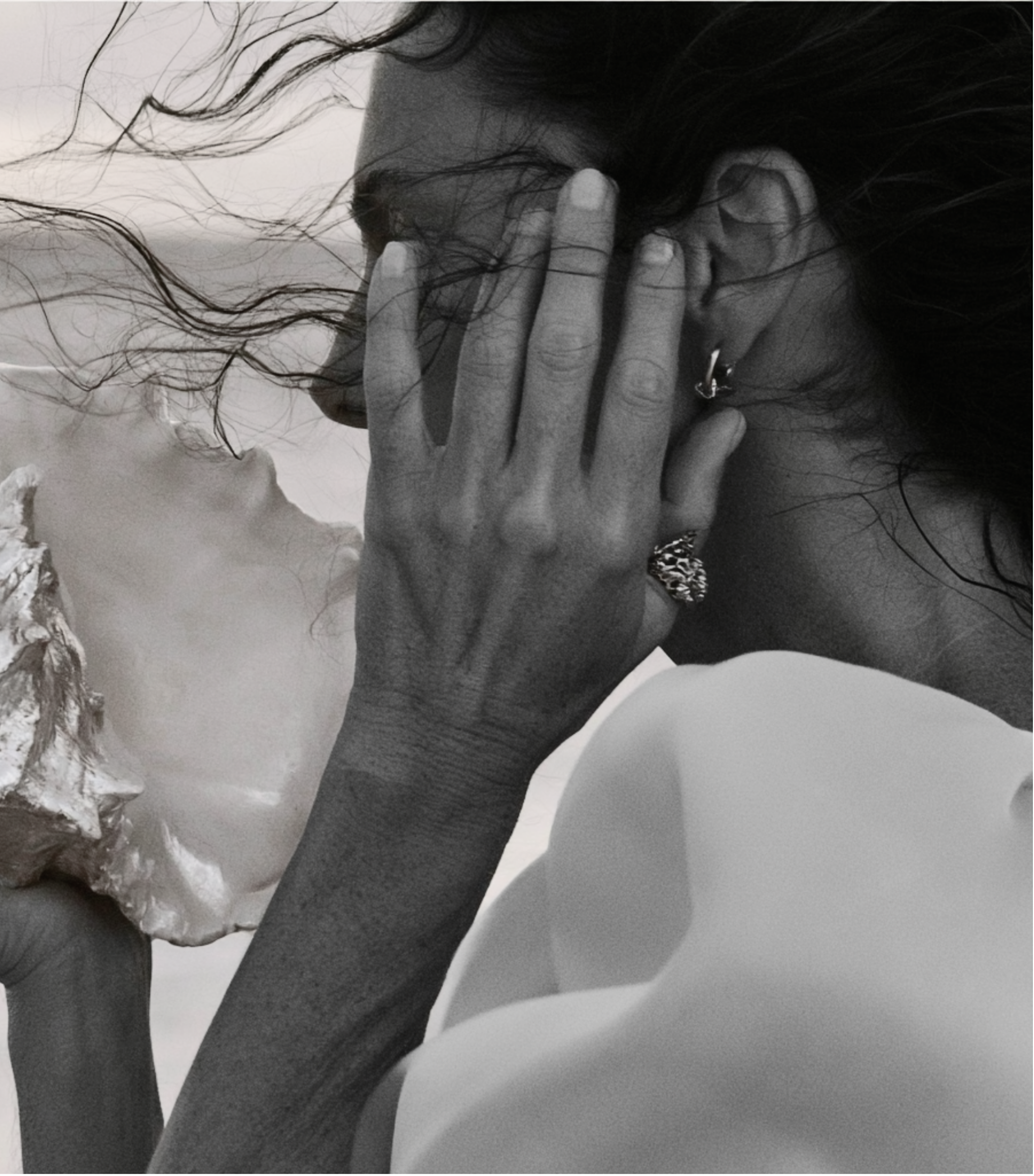 A person with dark, wavy hair and earrings touching another person's face with wavy hair, in a close, intimate moment, both with light skin tones.