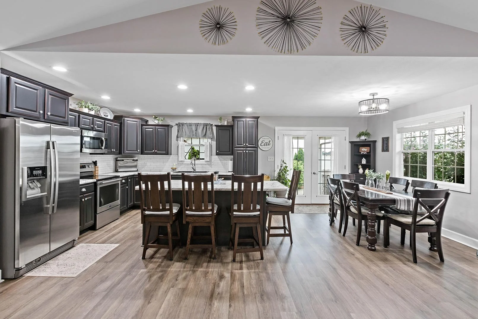 Modern kitchen and dining area with dark cabinetry, stainless steel appliances, and wooden flooring.
