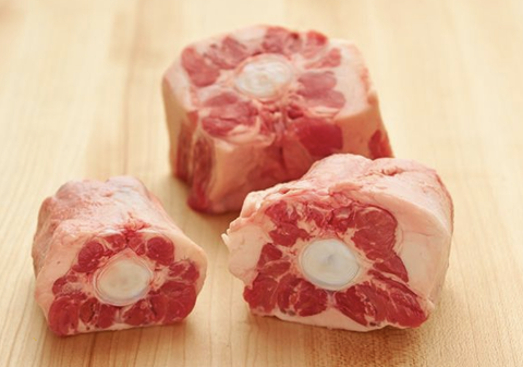 Three oxtail bones on a wooden cutting board.