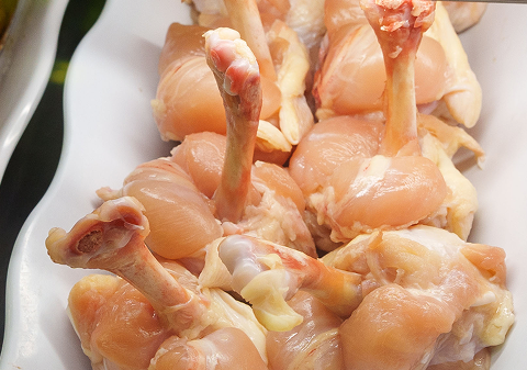 Raw chicken drumsticks on a white plate.