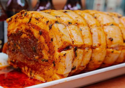 Close-up of a roasted pork roll stuffed with herbs, sliced and placed on a white platter.