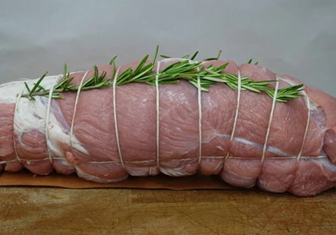 Rolled and tied raw pork tenderloin with sprigs of rosemary on a wooden cutting board.