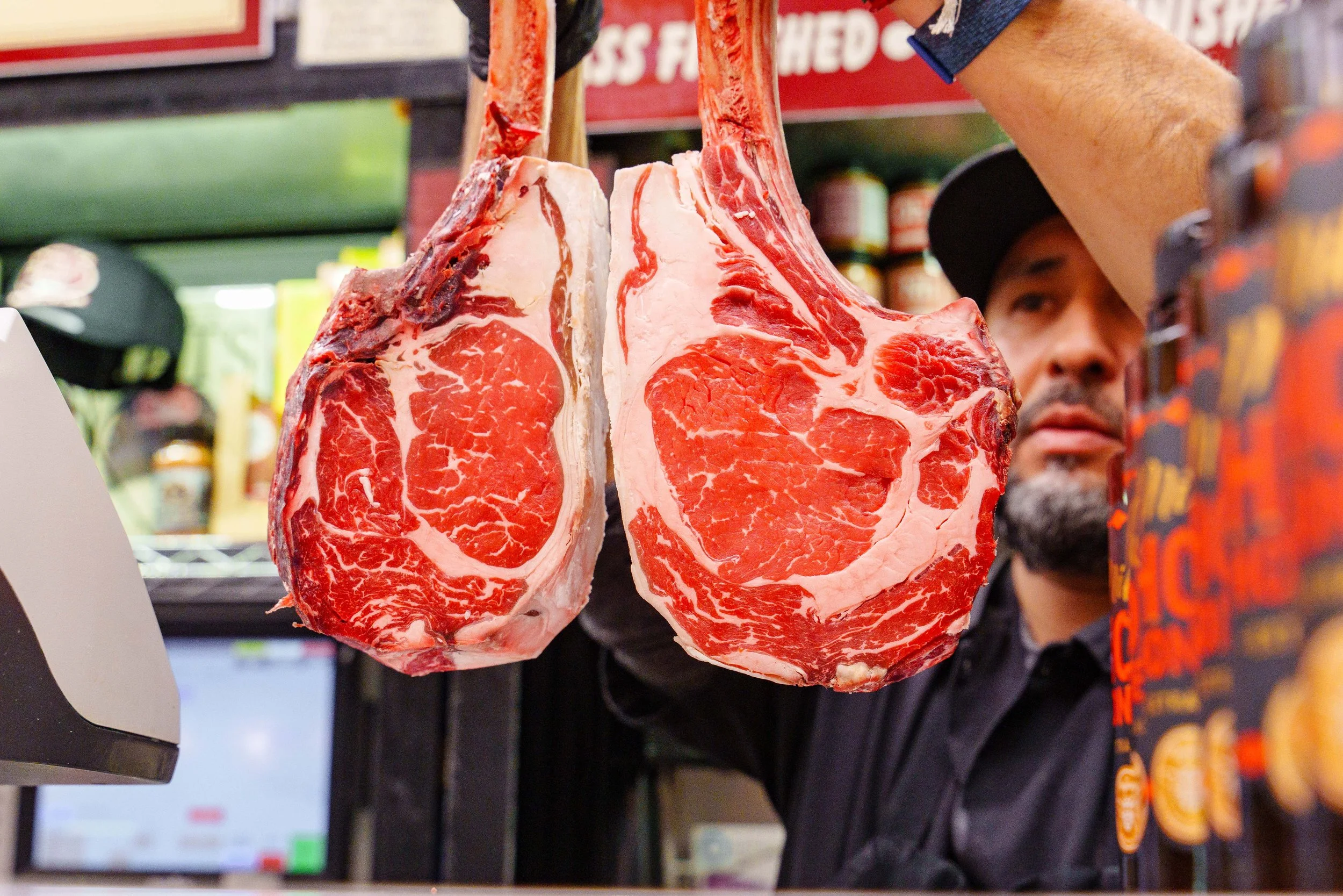 Butcher holding two large raw tomahawk steaks aloft.