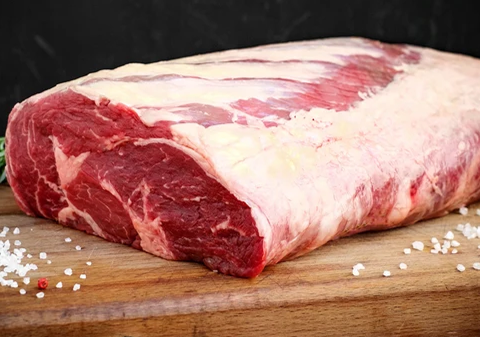 Raw meat on a wooden cutting board with salt and pepper.