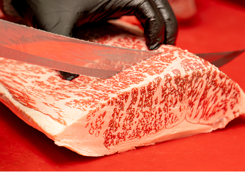 Close-up of a chef slicing a large piece of marbled Japanese Wagyu beef with a knife on a red cutting board.