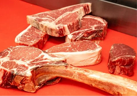 Various cuts of raw beef, including steaks and a large beef rib, on a red cutting board.