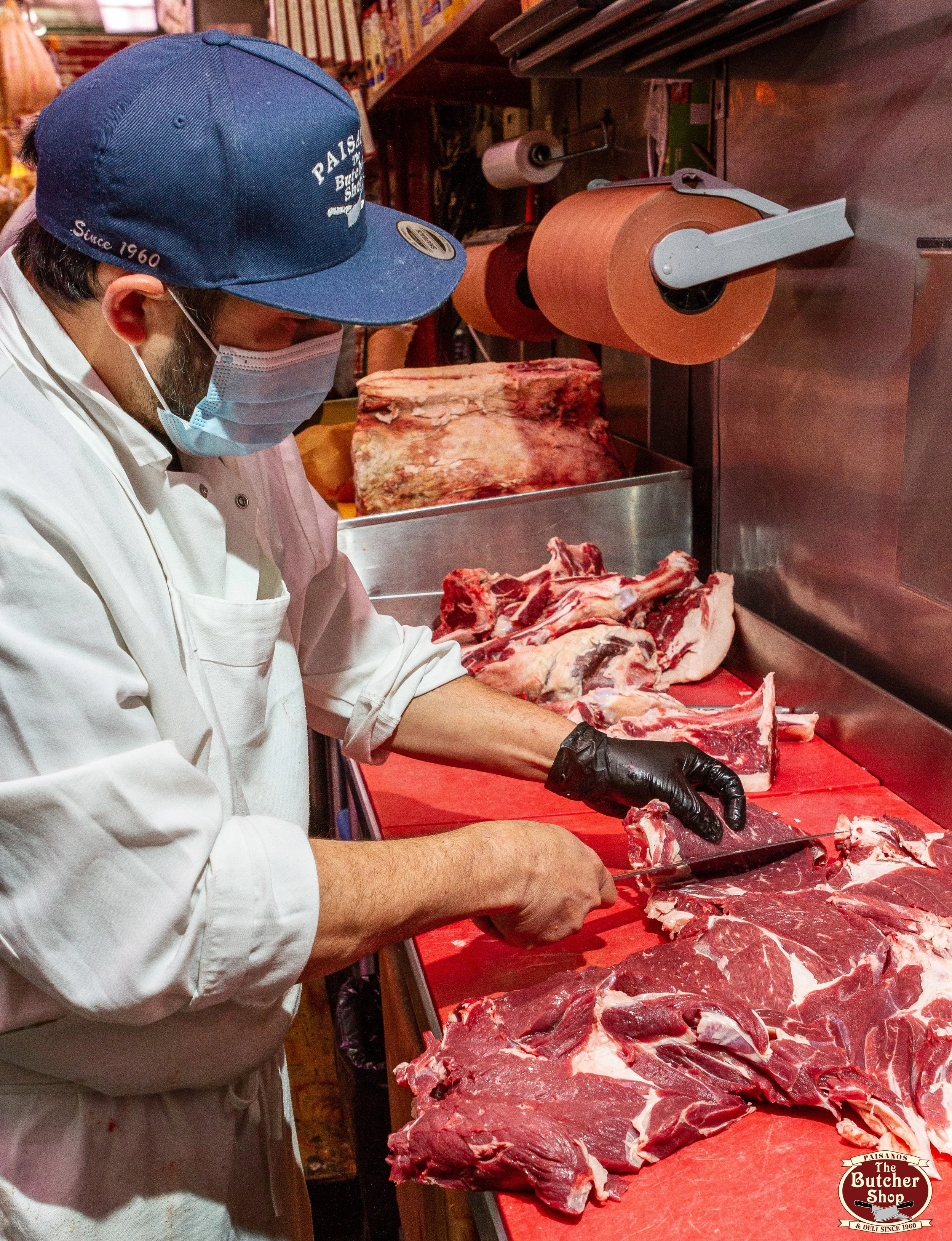 A butcher cutting large pieces of raw meat at a butcher shop counter displayed on a red countertop