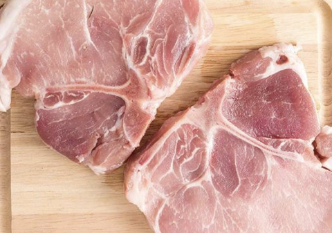 Two raw pork chops on a wooden cutting board.
