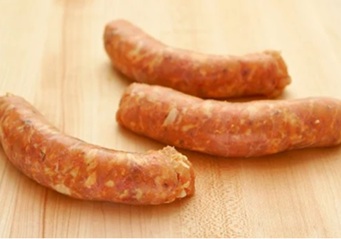 Three raw chicken sausage links on a wooden surface.