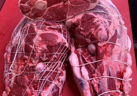 Raw lamb cuts tied with butcher's twine on a red surface.