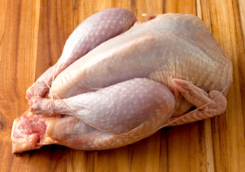 Raw, whole chicken on a wooden cutting board.