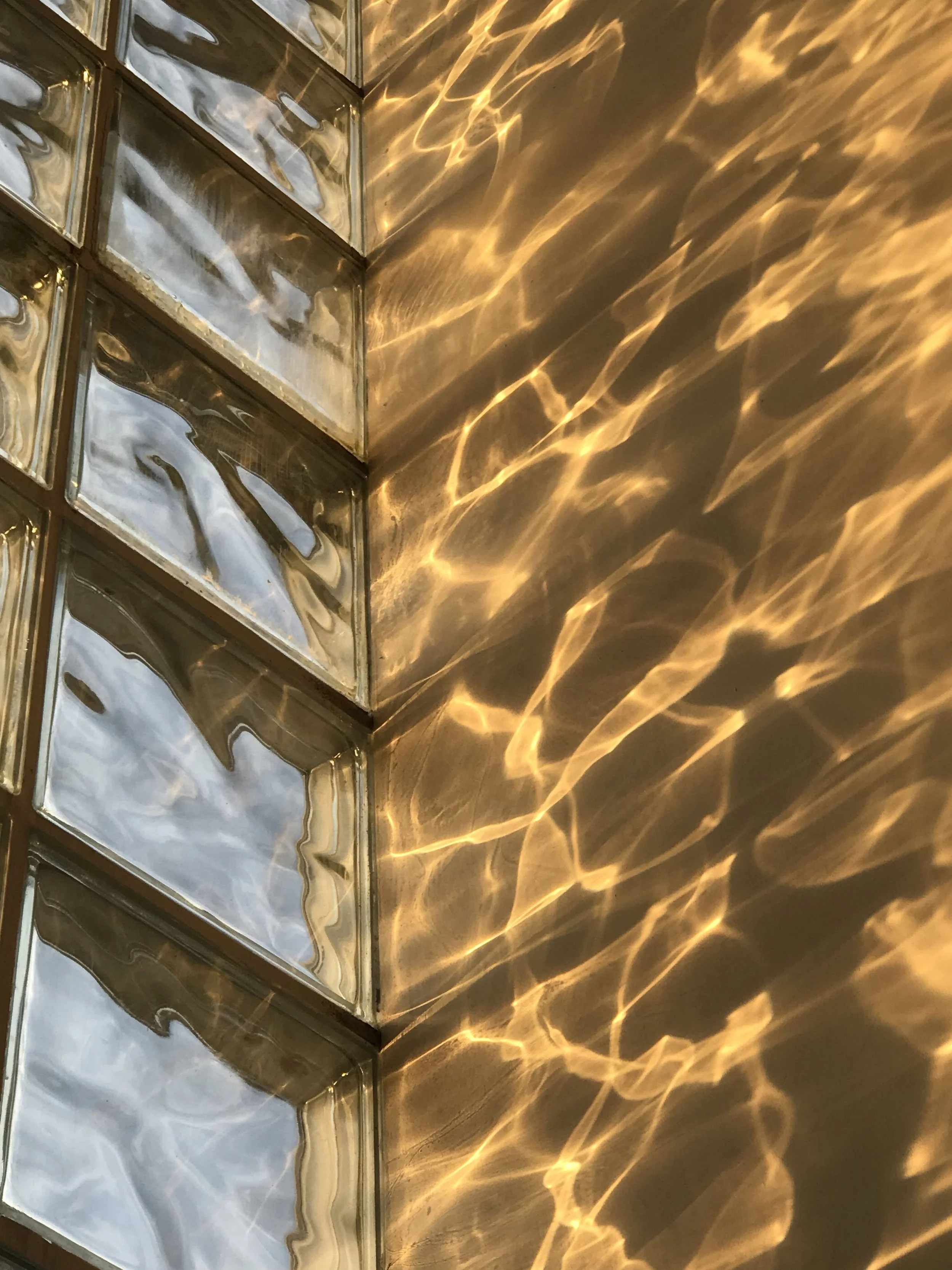 Reflections of light on a metallic surface, with a section of vertical glass blocks on the left side.