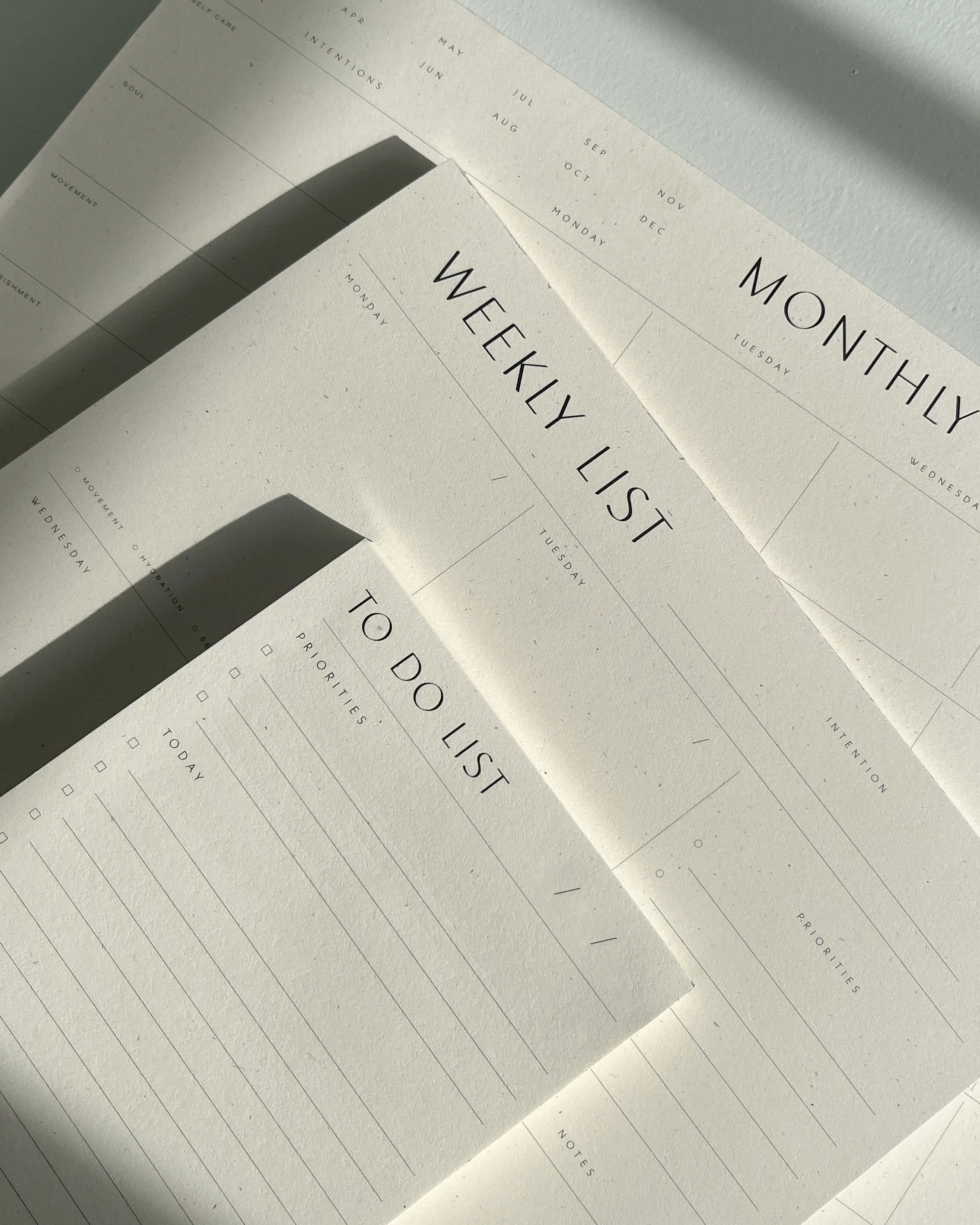 Close-up of a minimalist weekly planner with a Monday to Sunday layout, featuring the title 'WEEKLY LIST' in black, on textured white paper with soft shadows and natural lighting.