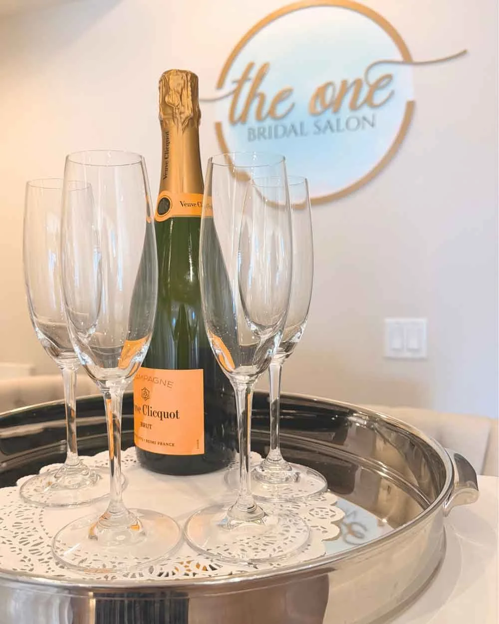 A champagne bottle and four champagne flutes on a silver tray at The One Bridal Salon.