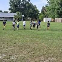 A group of people playing soccer on a grassy field with trees and a building in the background.