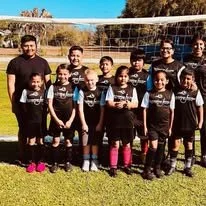 Youth soccer team posing on a field with their coach, all wearing black uniforms.