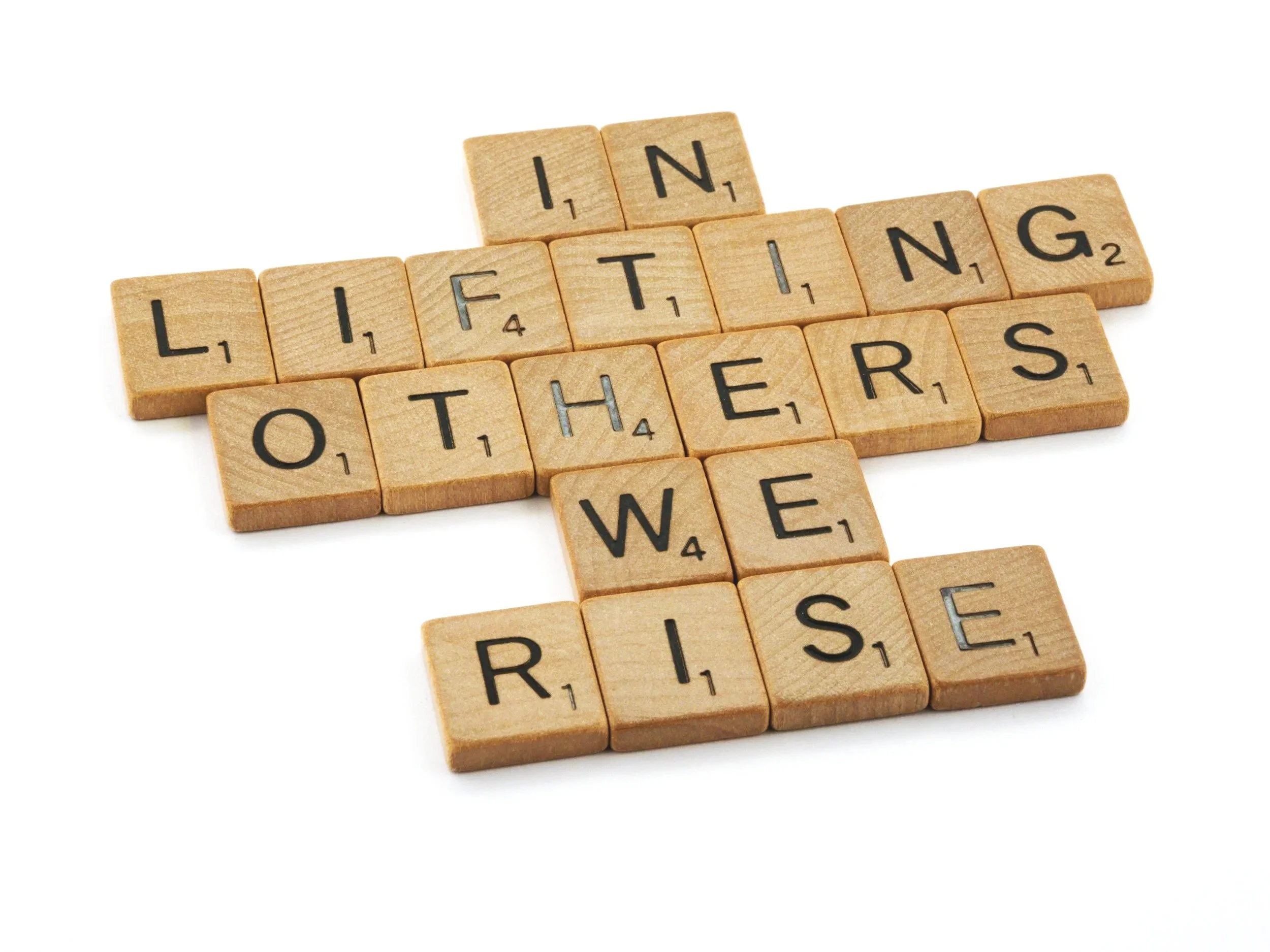 Wooden scrabble tiles spell out the phrase 'LIFTING OTHERS'.